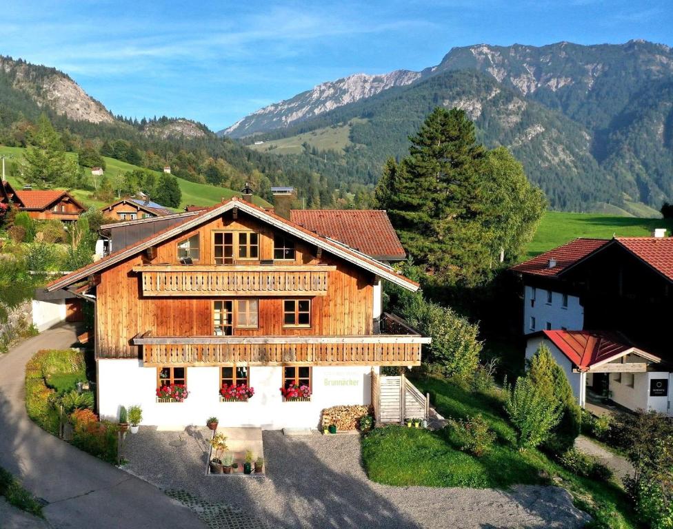 a large wooden house with mountains in the background at Ferienwohnung Brunnäcker in Bad Hindelang
