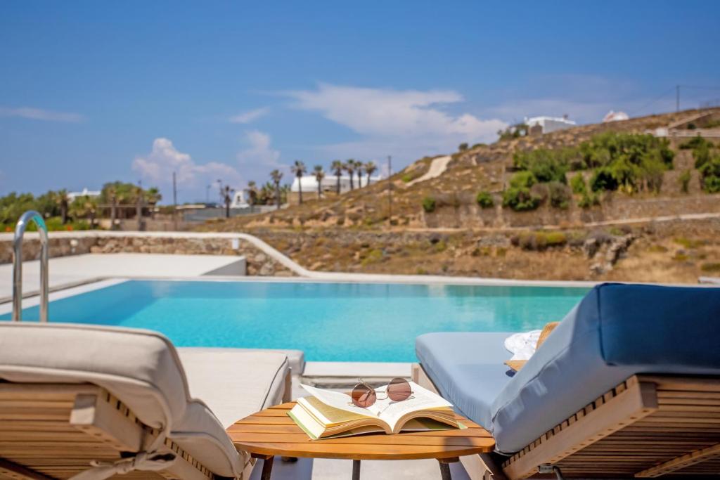 a pool with a chair and a table with a book at Aqua Breeze Seaview Pool Suites Mykonos in Mýkonos City