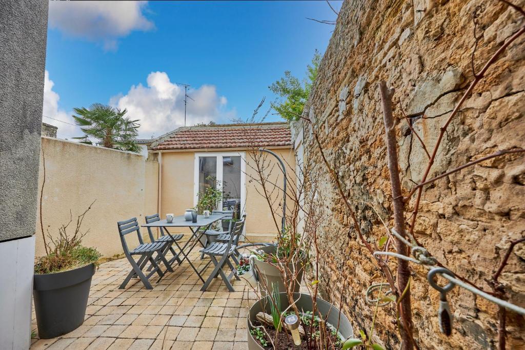 a patio with a table and chairs next to a stone wall at Cottage Côté Mer - A 1km de la plage in Courseulles-sur-Mer