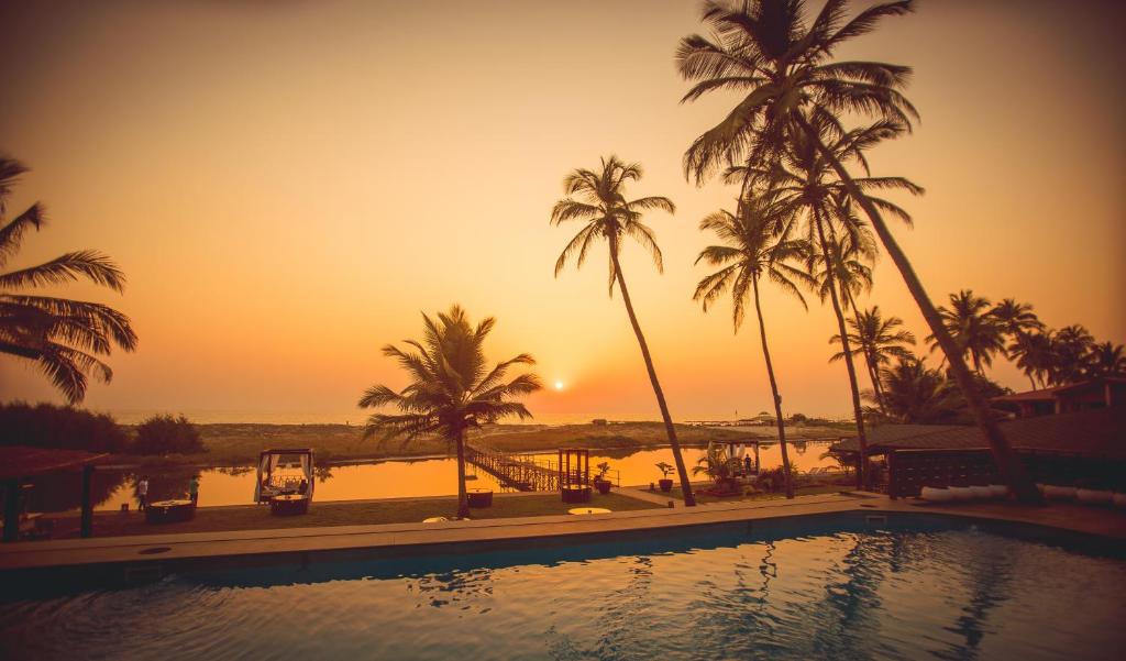 une piscine avec des palmiers et un coucher de soleil en arrière-plan dans l'établissement Riva Beach Resort, à Mandrem