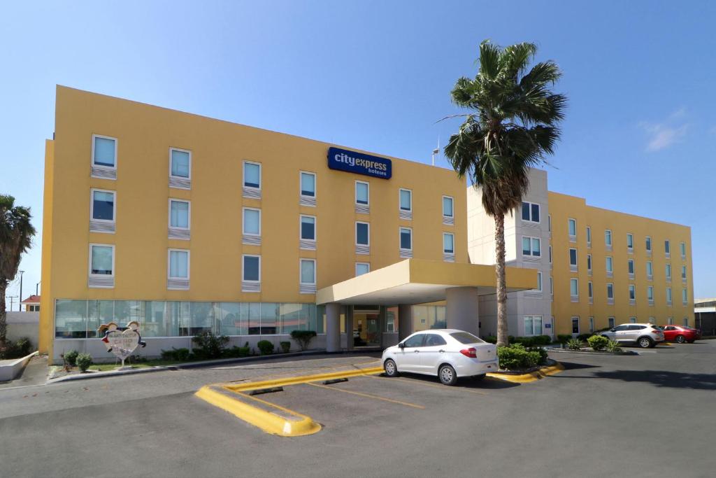un bâtiment jaune avec une voiture garée dans un parking dans l'établissement City Express by Marriott Nuevo Laredo, à Nuevo Laredo