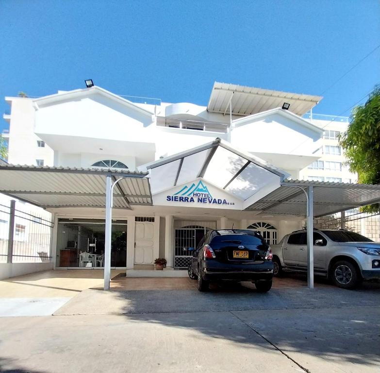 a white building with two cars parked in a parking lot at Hotel Sierra Nevada B&B SAS in Valledupar