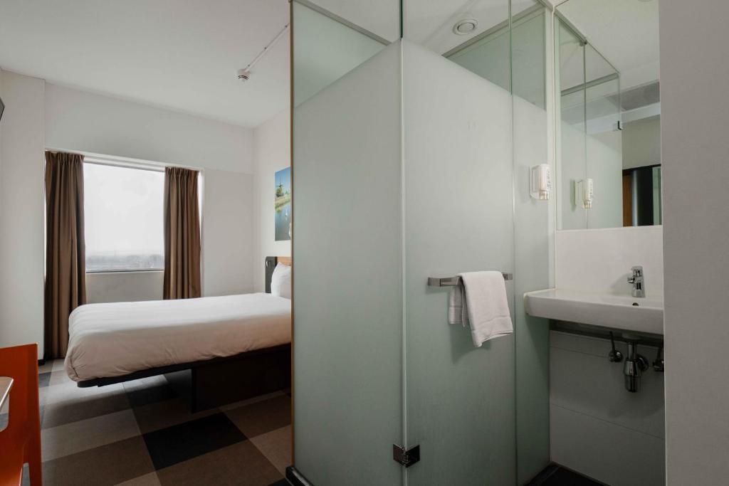 a bathroom with a bed and a sink and a mirror at easyHotel Amsterdam Zaandam in Zaandam