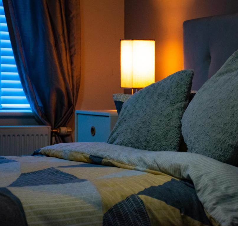 a bedroom with a bed with pillows and a lamp at Cosy Modern Flat (NEC/BHX Stays) in Marston Green