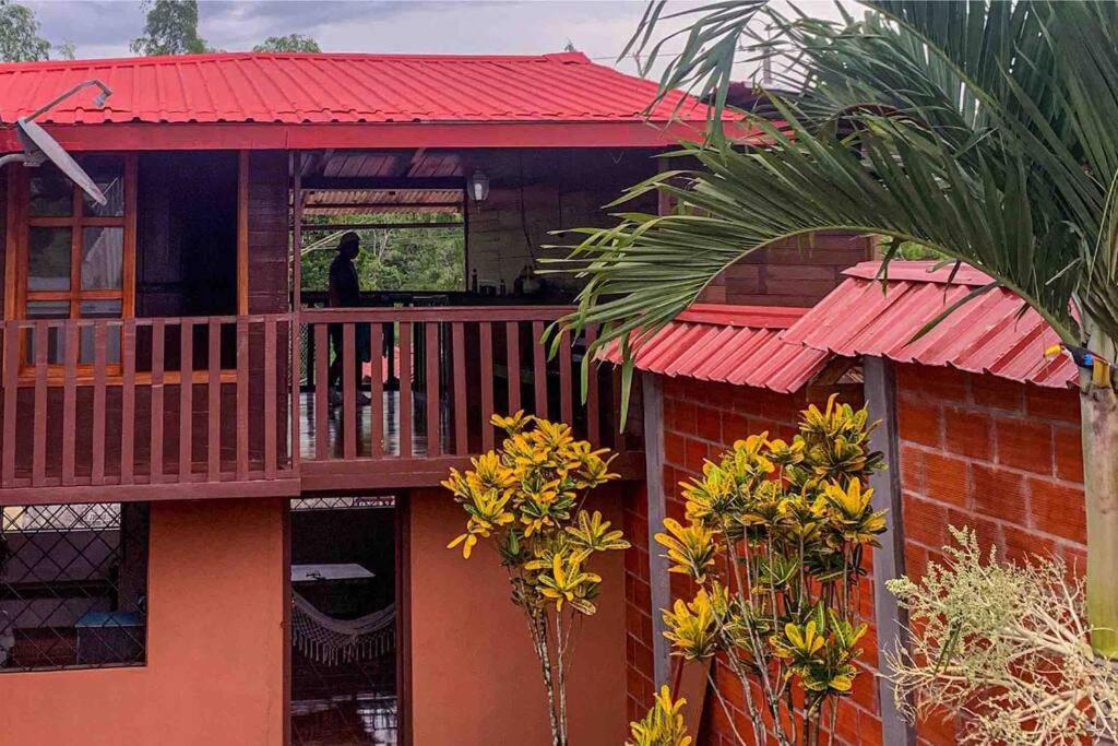 een huis met een rood dak en een persoon op een balkon bij Casa en Misahualli - Misahualli HOME in Puerto Misahuallí