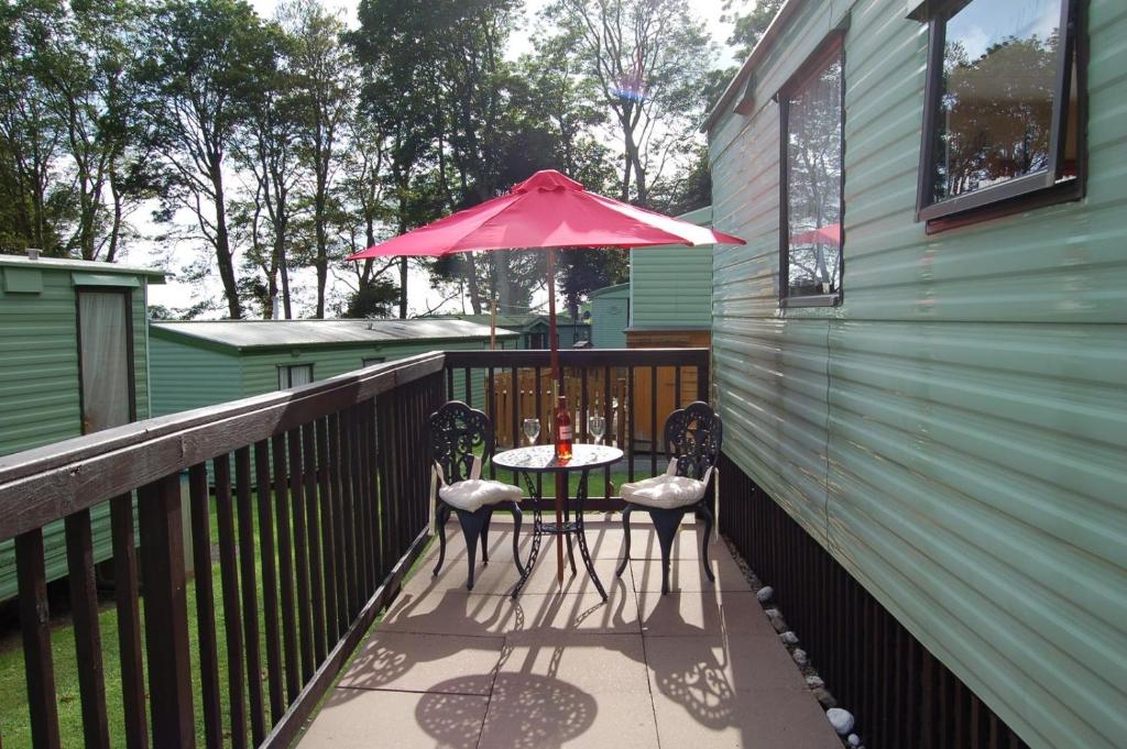 a table and chairs on a balcony with an umbrella at Caravan B26 at The Woodlands in Tywyn