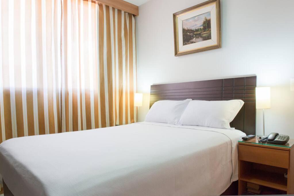 a bedroom with a large white bed and a telephone at Monumental Nobile- Apart hotel Central in Brasilia