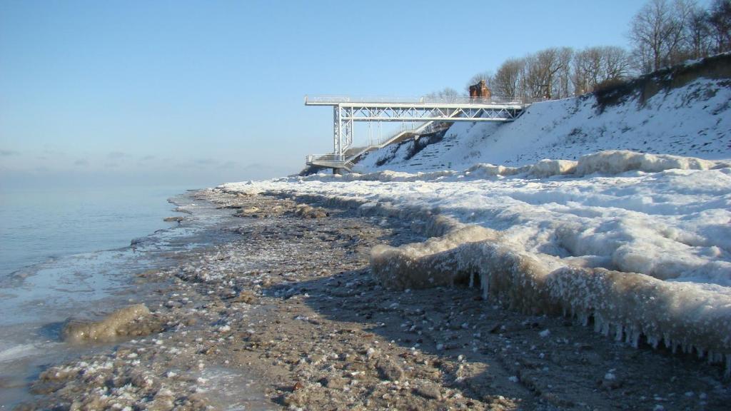 a snow covered shore with a bridge in the background at Aparthouse Cliff by Orka in Trzęsacz