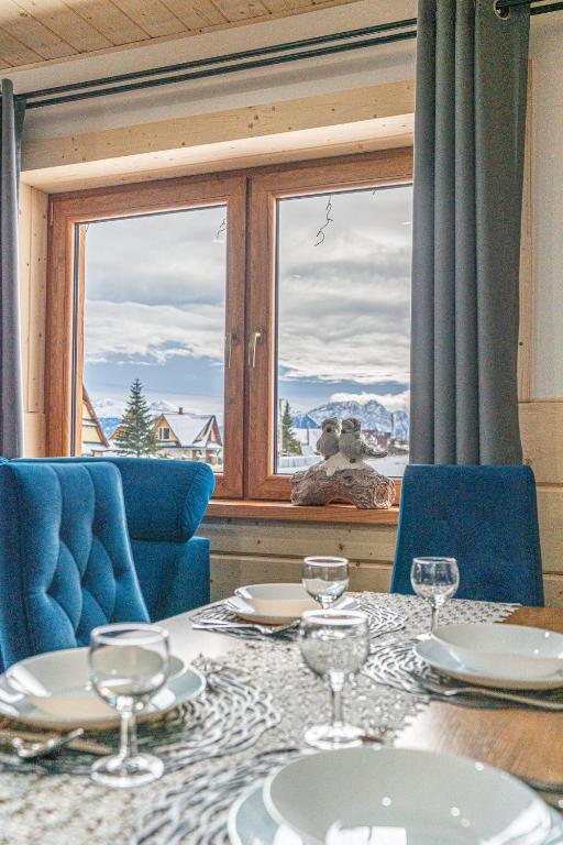 a table with glasses and blue chairs and a window at Domki na Wiyrchu in Biały Dunajec