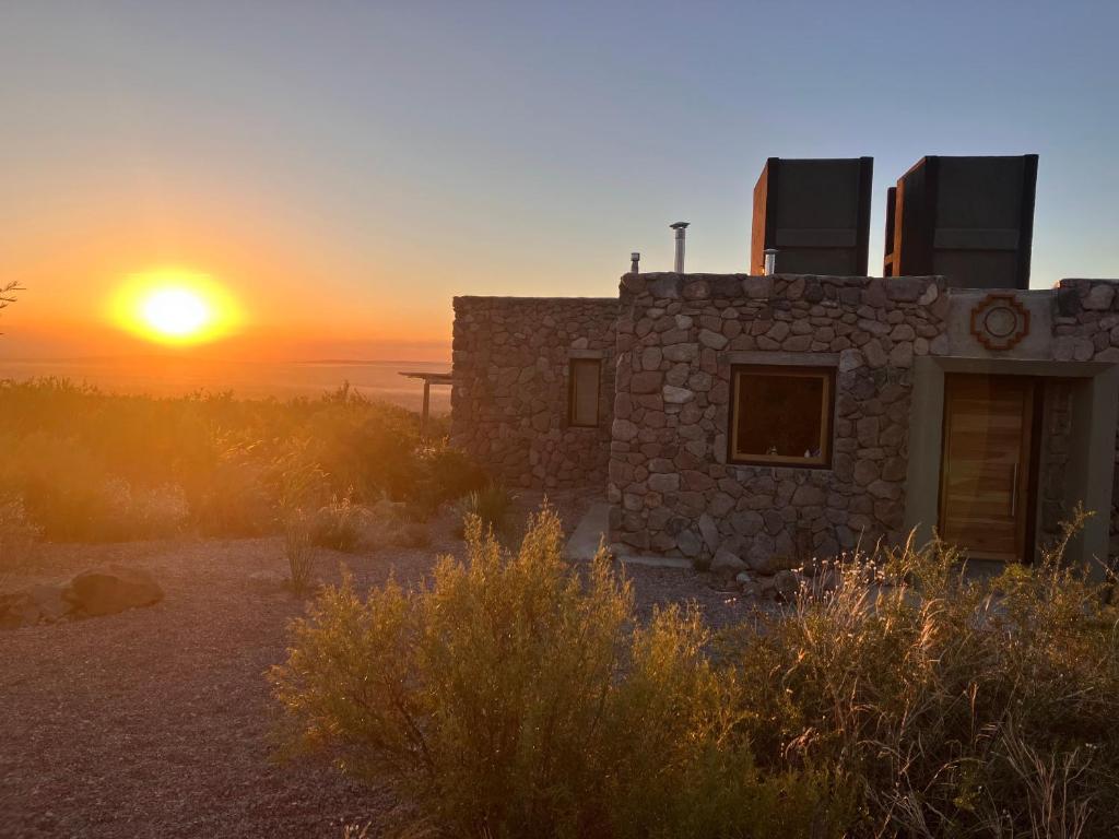 盧漢德庫約的住宿－Bendita Piedra Suites, Las Compuertas Lujan de Cuyo，一座石头房子,背景是日落