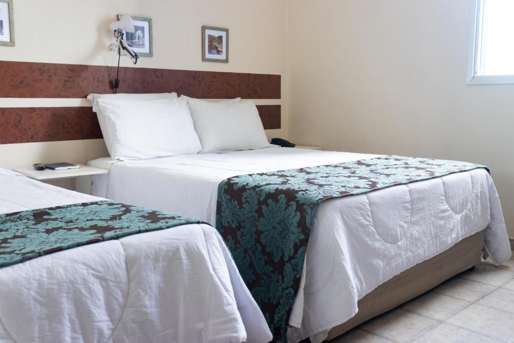 um quarto com 2 camas e lençóis brancos em Hotel Minastur em Capitólio