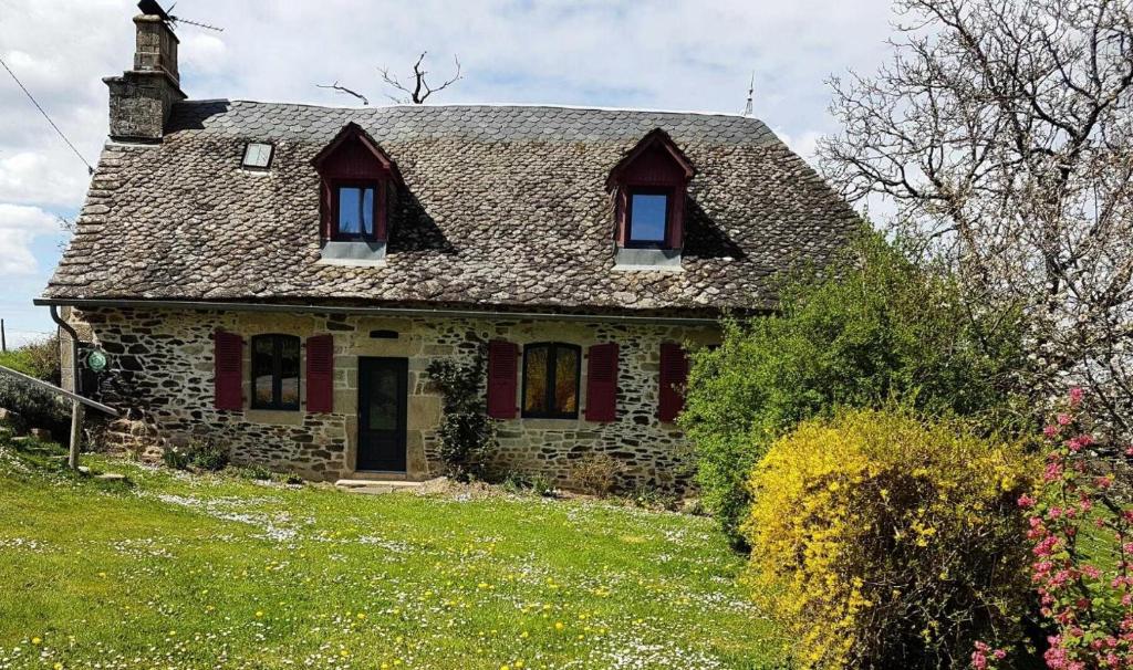 ein altes Steinhaus mit roten Fenstern und einem Dach in der Unterkunft Gîte de France à Saint-Martin-la-Méanne 2 épis - Gîte de France 5 perso 854 in Saint-Bazile-de-la-Roche