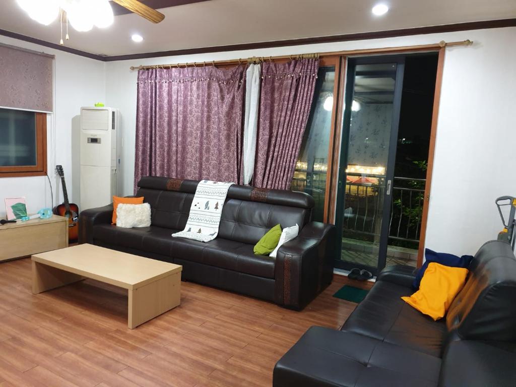 a living room with a black leather couch and a table at Camp Humphreys pyeongtaek's sharing house in Pyeongtaek