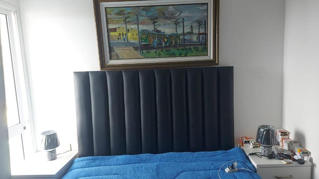 a bedroom with a bed with blue sheets and a painting at Apartamento frente mar - Barra da Tijuca in Rio de Janeiro