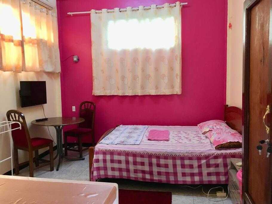 a bedroom with a pink wall with a bed and a table at Hotel Mangueira in Paramaribo