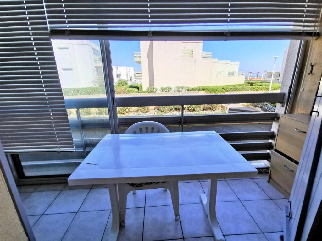 une table blanche et une chaise en face d'une fenêtre dans l'établissement Résidence LE CARLTON - 2 Pièces pour 4 Personnes 04, à Port-Leucate
