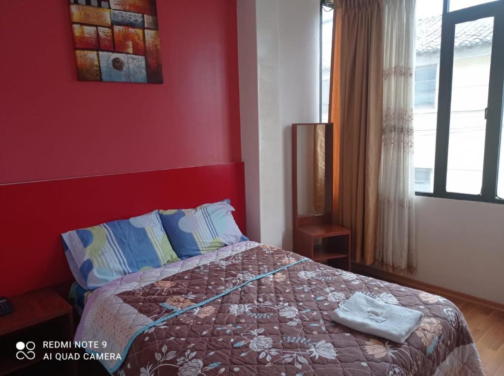 1 dormitorio con cama y pared roja en Hotel RITZOR, en Latacunga