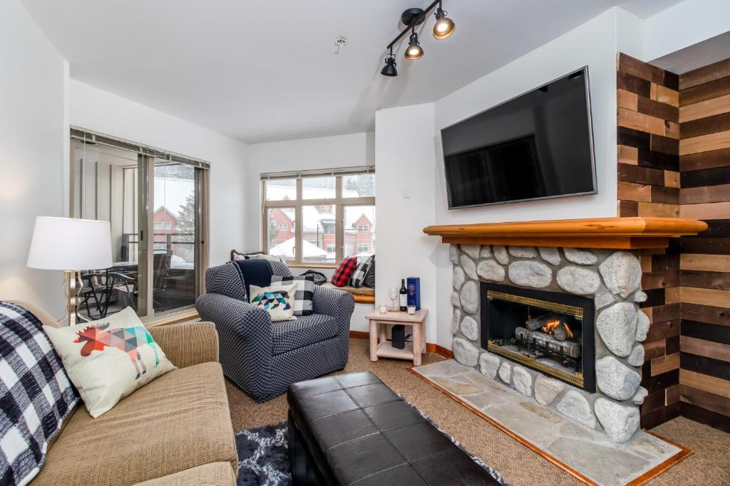 a living room with a fireplace with a tv above it at Creekside Slopeside 1BR with pool, hot tub, BBQ in Whistler