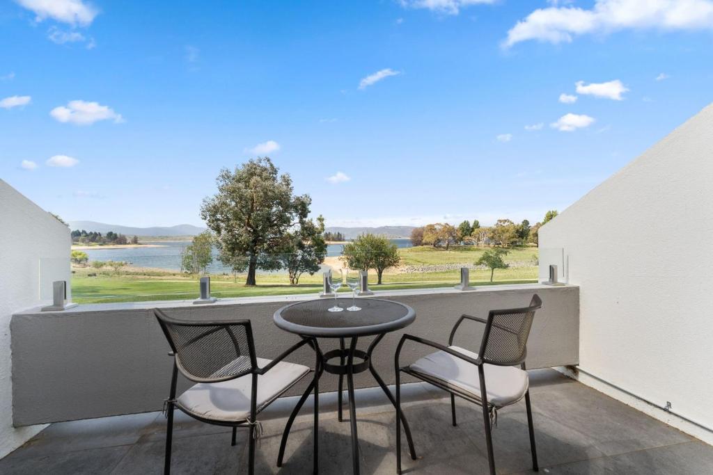 a balcony with a table and chairs and a view of the water at Horizons 414 - Deluxe Lake Front Studio l Pool l Tennis l WiFi in Jindabyne