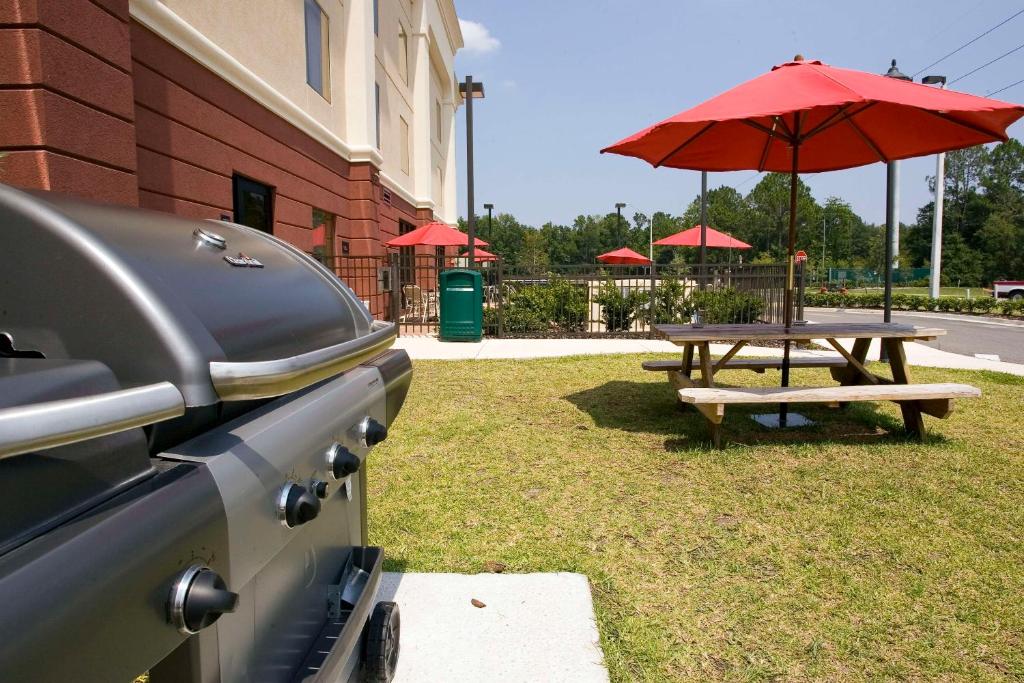 a picnic table with a red umbrella next to a building at Hampton Inn Jacksonville I-10 West in Jacksonville