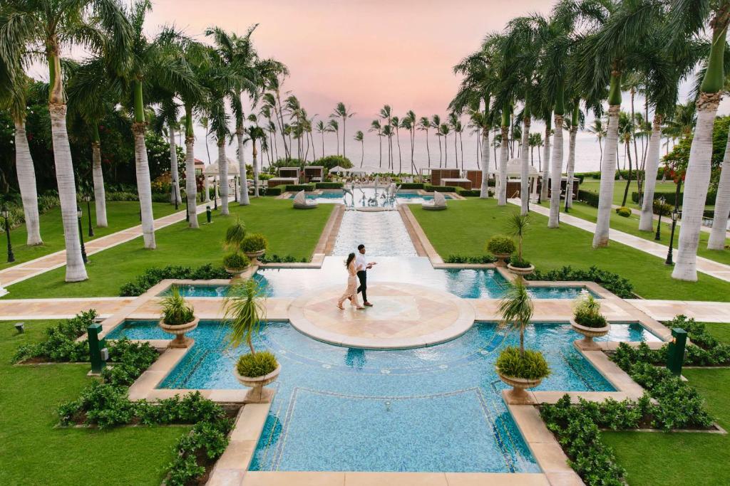 a couple stands in front of a fountain in a park with palm trees at Grand Wailea Resort Hotel & Spa, A Waldorf Astoria Resort in Wailea
