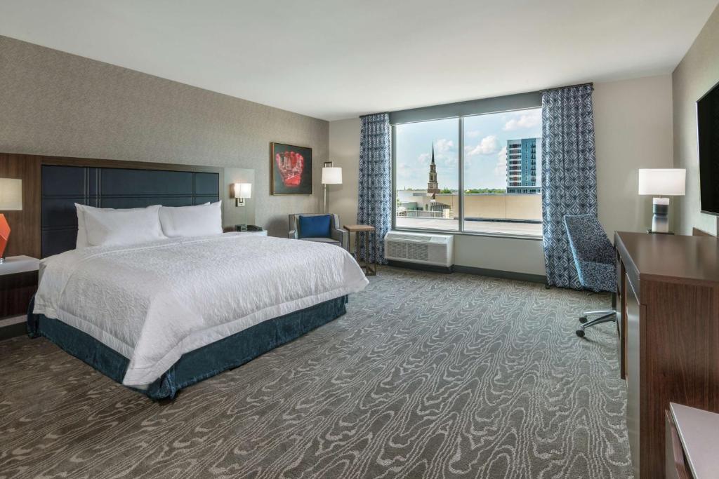 フォートウェインにあるHampton Inn & Suites Fort Wayne Downtownのベッドと大きな窓が備わるホテルルームです。