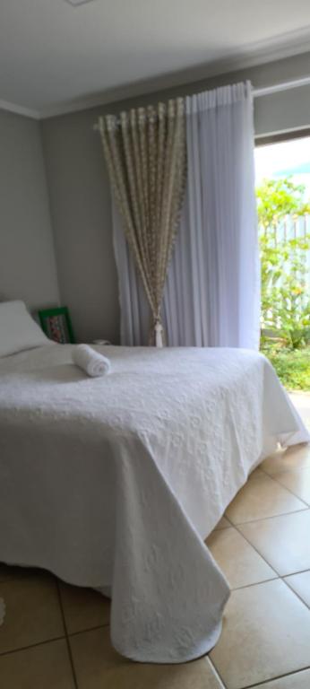 uma cama branca num quarto com uma janela em Quarto Luz em Jaraguá do Sul