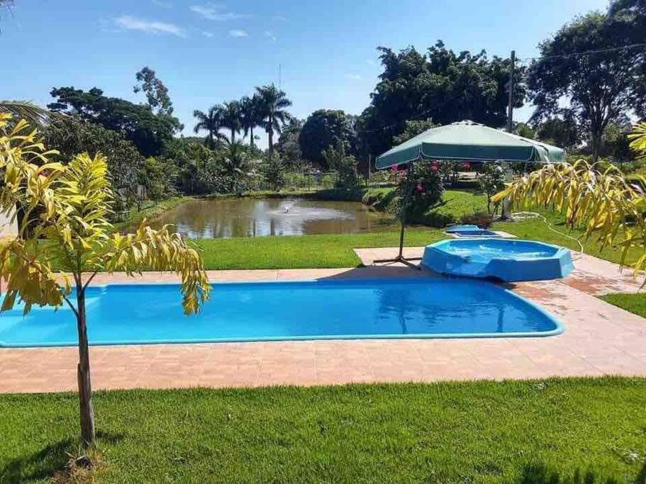 a swimming pool with an umbrella next to a pond at Chácara de Lazer 2 Lagoas in Nova Esperança