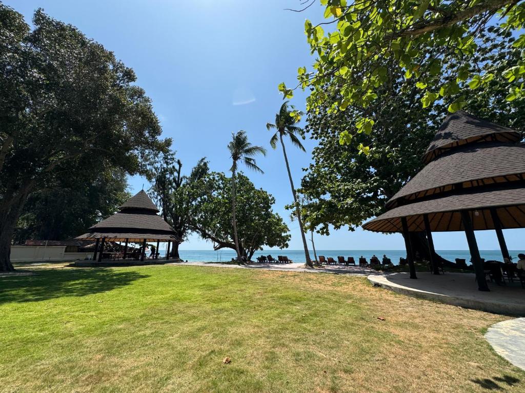 a beach with umbrellas and people sitting on the grass at Beach Bungalow at Lanta Resort in Ko Lanta