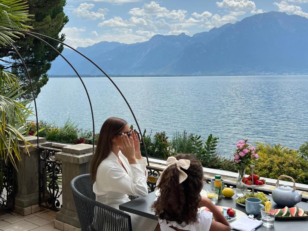 kobieta i dziecko siedzące przy stole nad wodą w obiekcie Montreux Luxury Suite w mieście Montreux