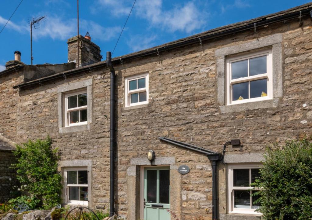 een oud stenen huis met witte ramen en een schoorsteen bij The Cottage in Thwaite