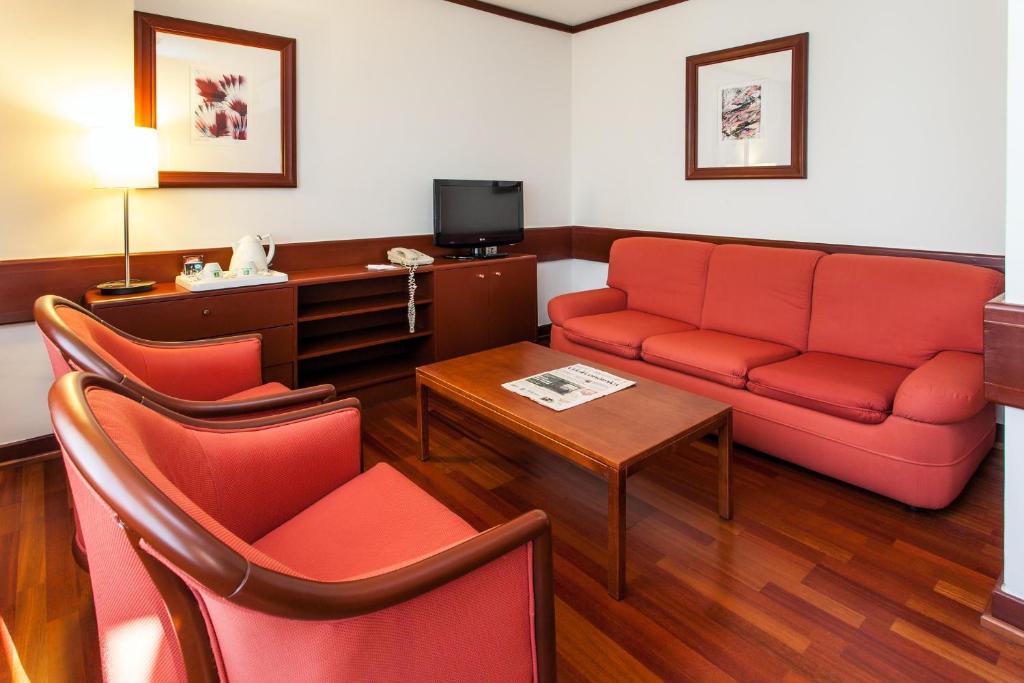 A compact sitting area with a red sofa, two armchairs and a television.