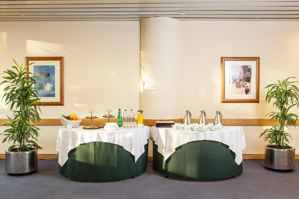 Two round buffet tables stand between potted plants in a carpeted event area.