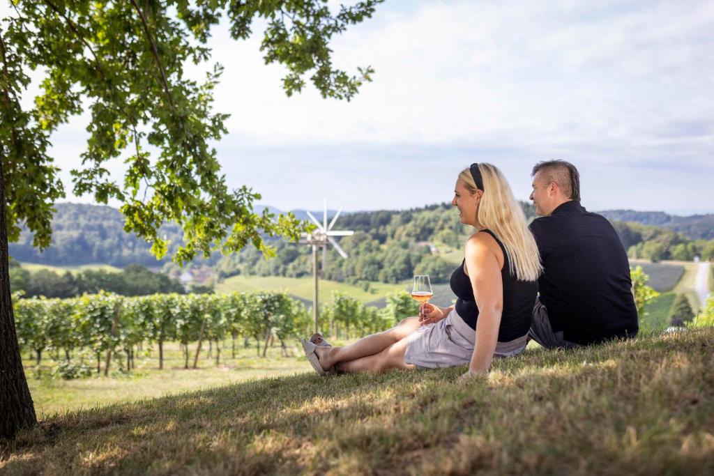 mężczyzna i kobieta siedzący na wzgórzu z kieliszkiem wina w obiekcie Weingut Dietl w mieście Riegersburg