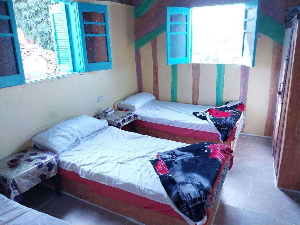 Habitación con 2 camas y 2 ventanas. en Azoz Nubian House, en Asuán