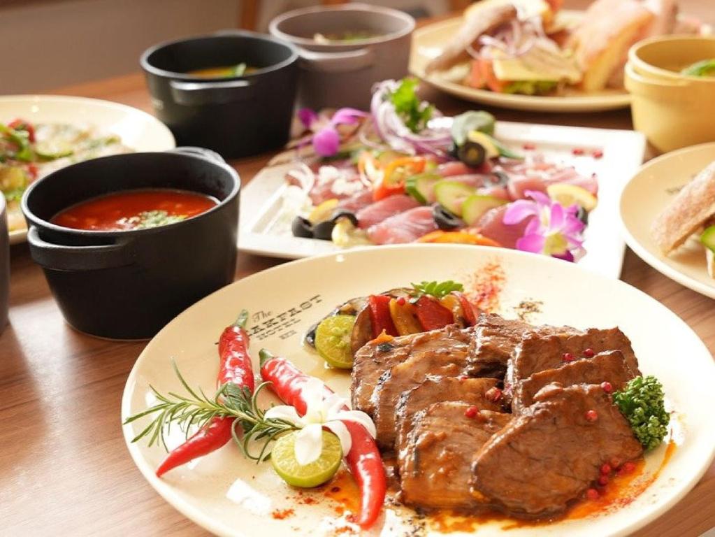 a table with plates of food with meat and vegetables at The BREAKFAST HOTEL MARCHE Ishigaki Island in Ishigaki Island