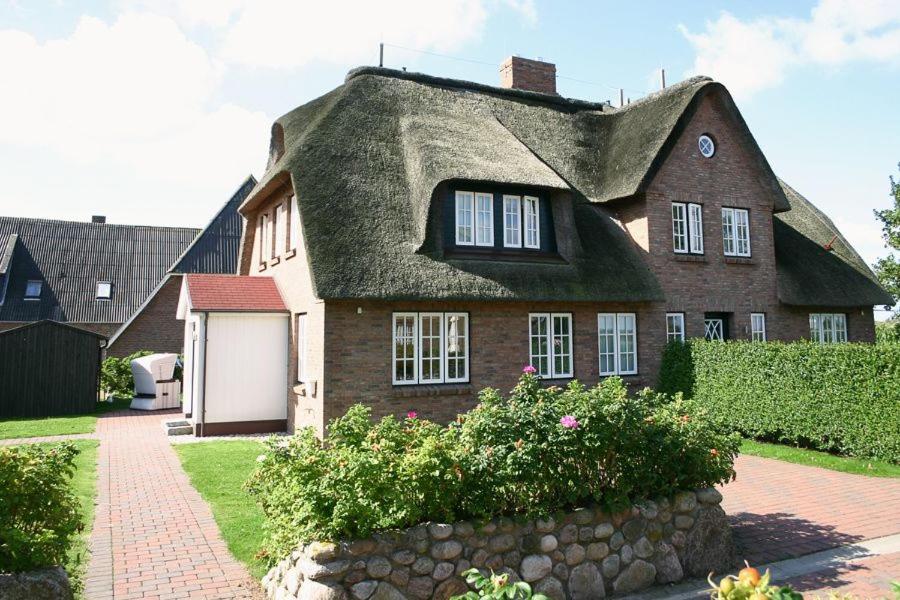 a house with a thatched roof and a stone wall at Haus Grünland in Alkersum