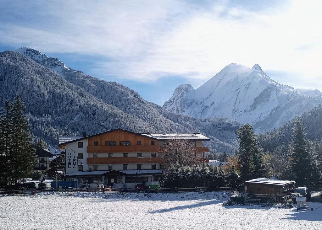 a building in the snow with mountains in the background at Dolomiten Hotel Irma in Canazei