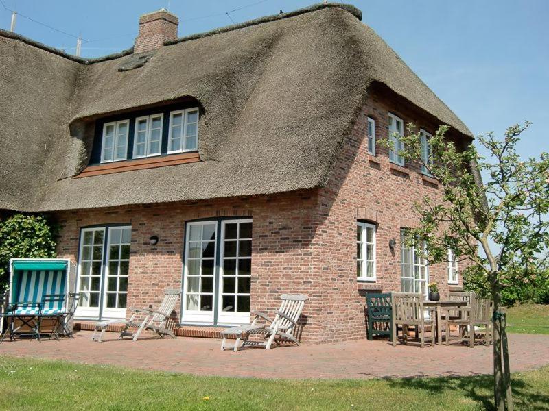 a brick house with a thatched roof with chairs at Haus Traumstraße in Hedehusum