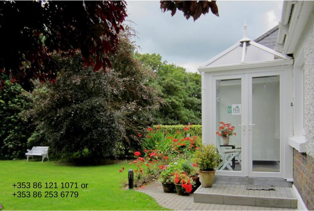 a whiteconservatory in a garden with flowers and plants at Conways B&B in Claremorris