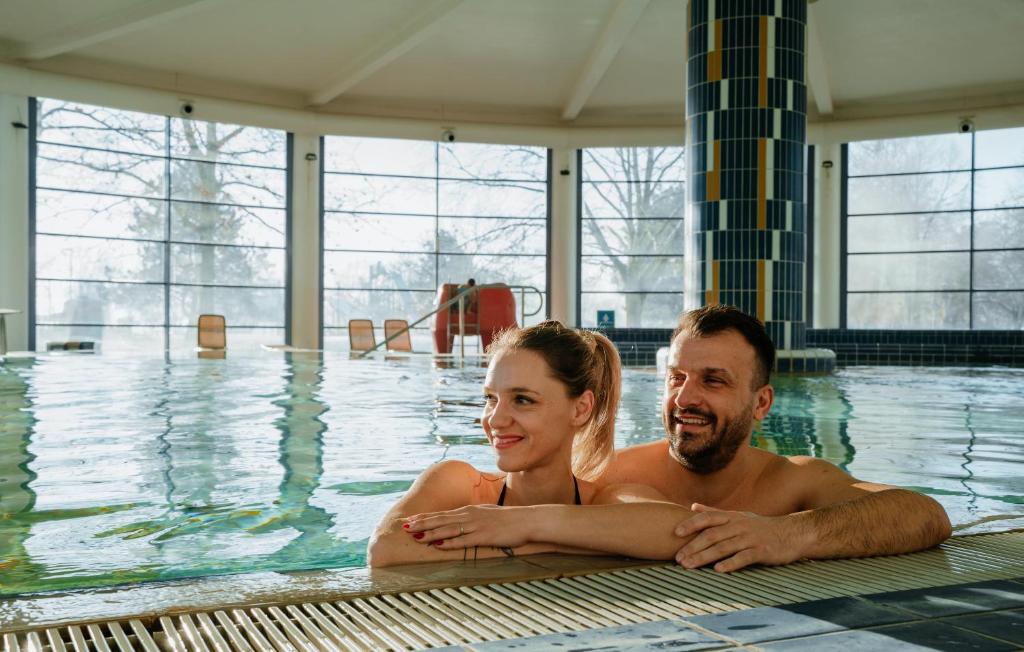 a man and woman laying in a swimming pool at Thermal Resort Hotel Lendava in Lendava