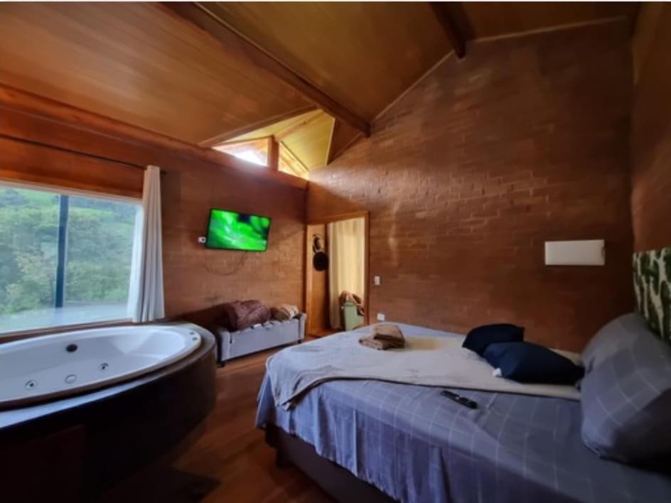 a bedroom with a bed and a tub and a tv at Chalé Jequitibá- Valedaspedrasmg in Sapucaí-Mirim