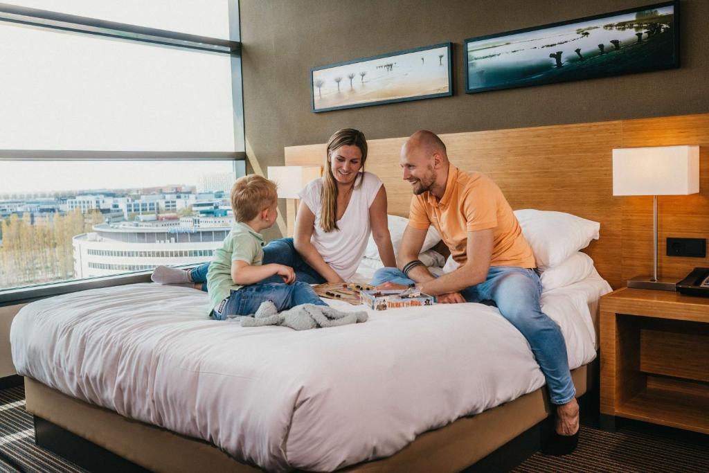 una familia sentada en una cama en una habitación de hotel en Hyatt Place Amsterdam Airport en Hoofddorp