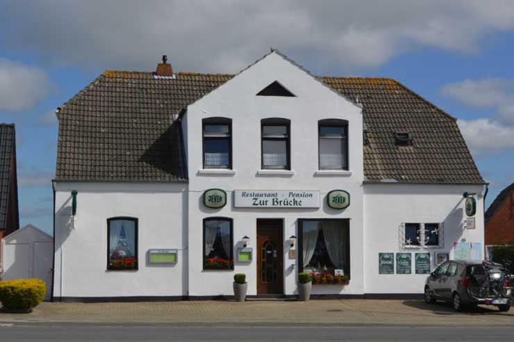 a white building with a car parked in front of it at Pension Restaurant Zur Brücke in Carolinensiel
