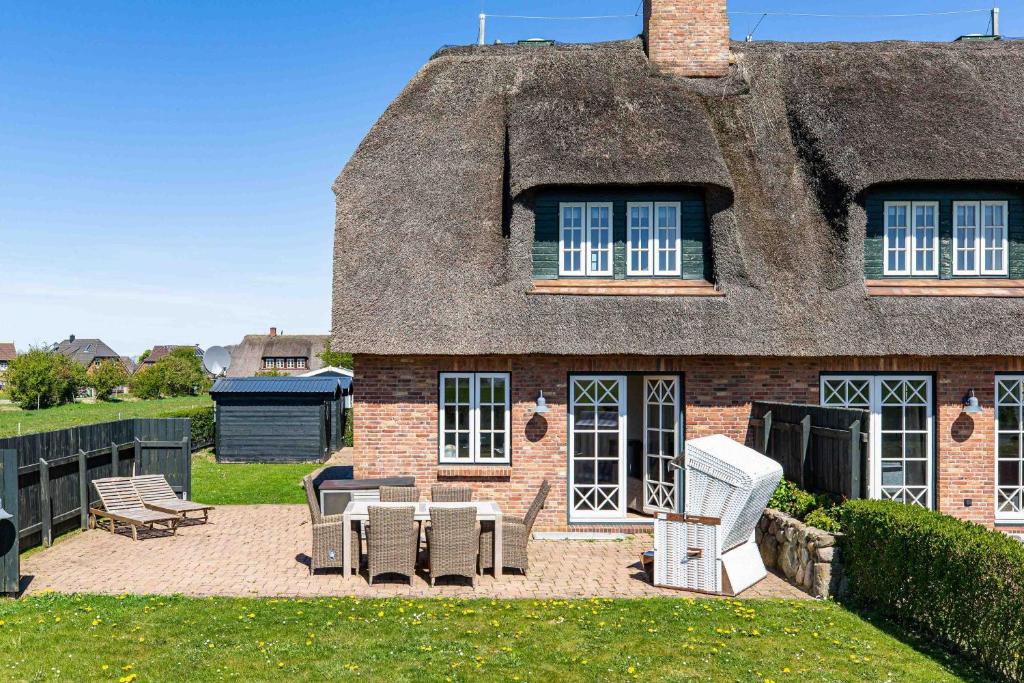 a house with a thatched roof with chairs and a patio at Stine Marie 2 in Borgsum