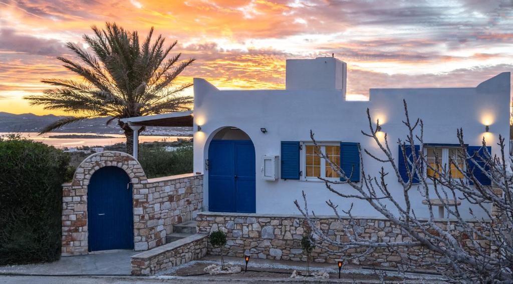 une maison blanche avec des portes bleues et un palmier dans l'établissement Noho Villas @ Sunlit house Paros, à Nea Cryssi Akti