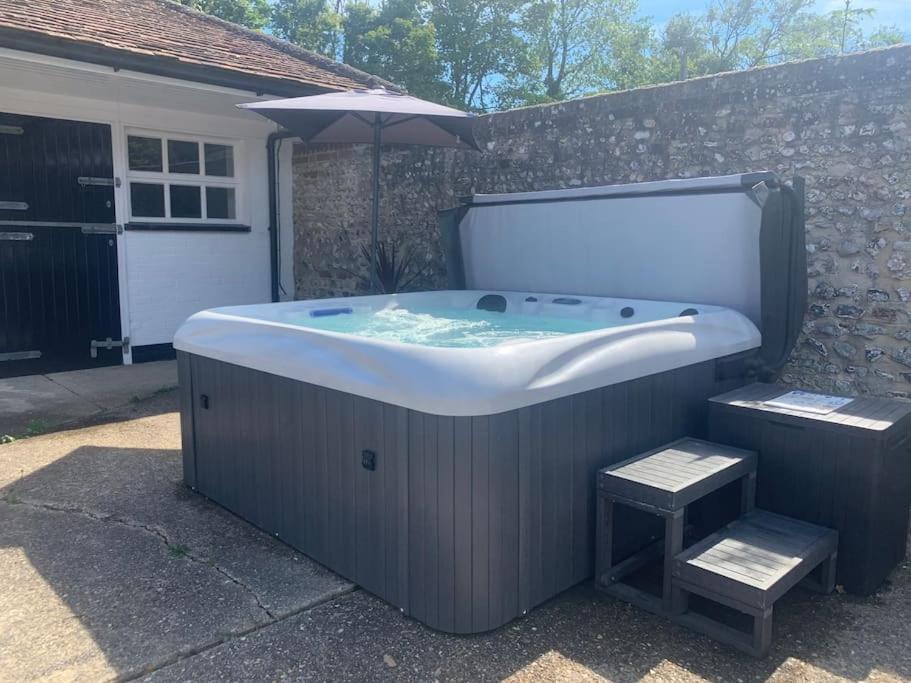 a large bath tub sitting in a yard with an umbrella at Chillout!! Sussex Flint Cottage- HotTub - Goodwood in Eartham