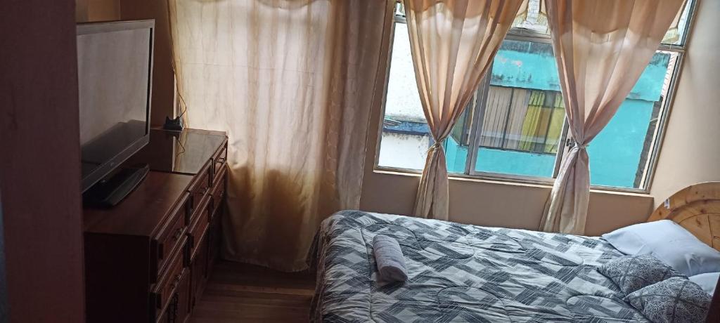 um quarto com uma cama, uma televisão e uma janela em Hospedaje Baños de Agua Santa em Baños