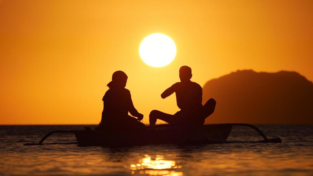 two people sitting on a boat in the water at sunset at Yuki Lodge - El Nido PH in El Nido