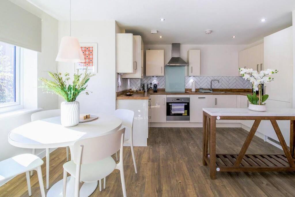 a white kitchen with a white table and chairs at Exquisite Apartment with Balcony, Free Parking, Fast WiFi, and Smart TV by Yoko Property in Milton Keynes